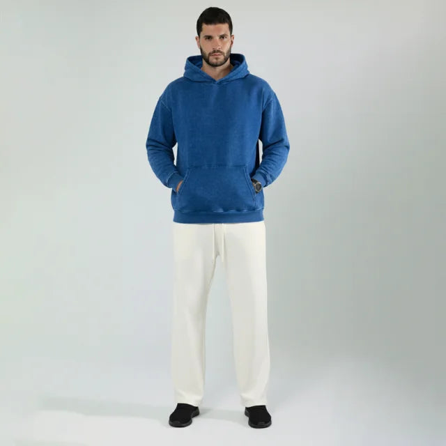 Man wearing a blue hoodie and white pants on a plain background  

